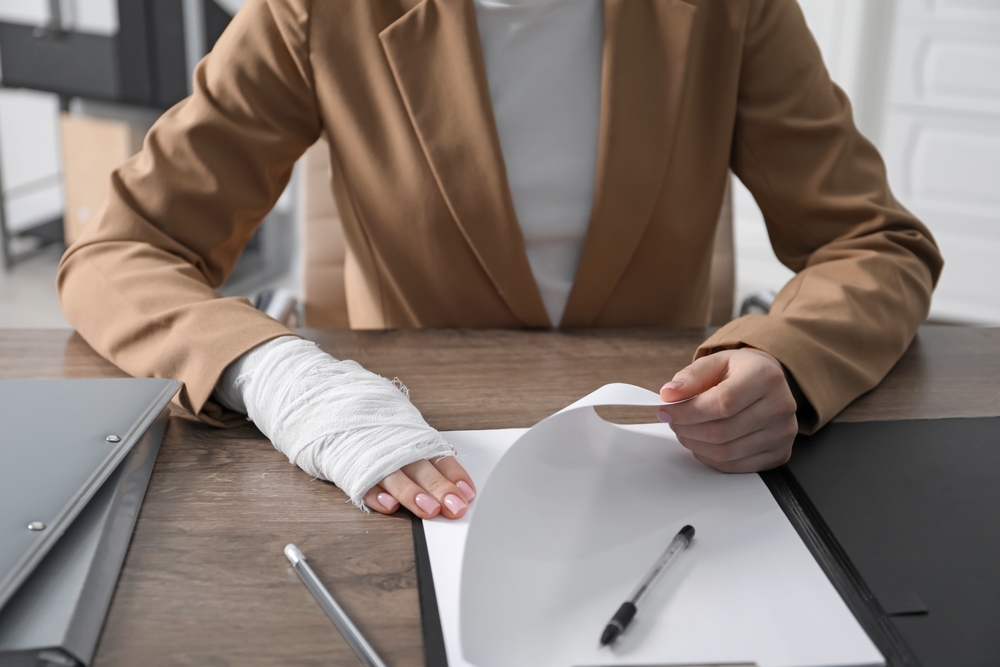 Woman with medical bandage on her wrist working at wooden table indoors,